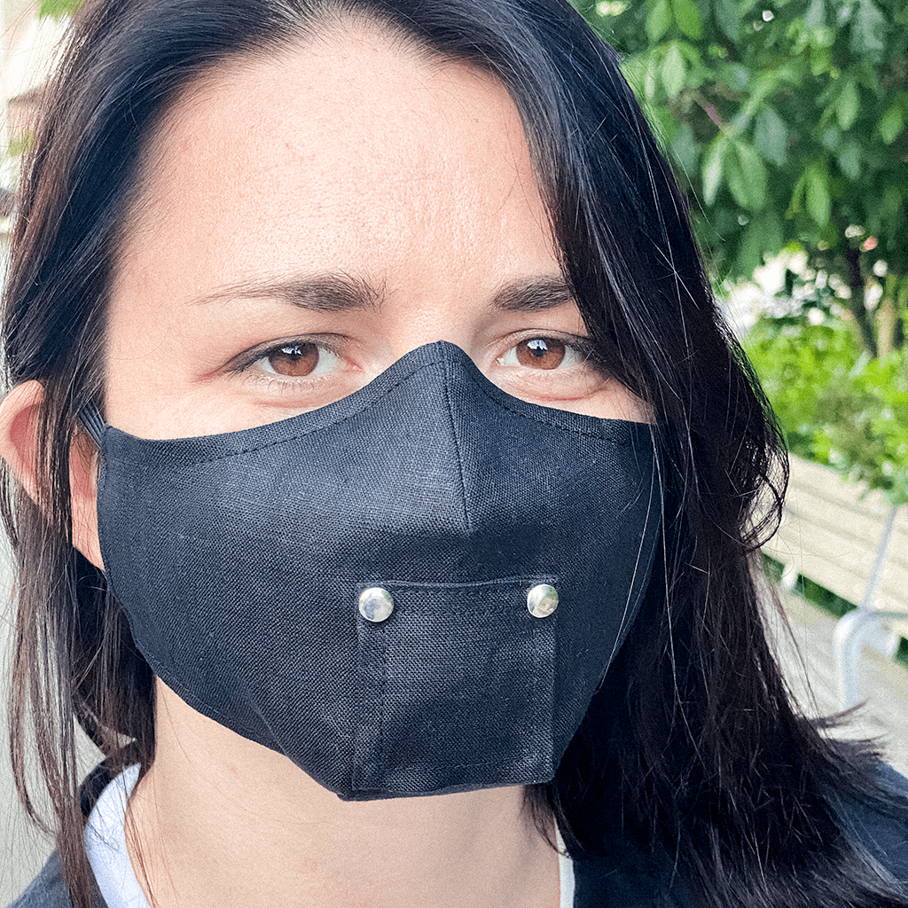 A stylish black face mask made from 100% organic linen, featuring a straw hole for easy sipping, adjustable elastic loops, and a moldable nose bridge.