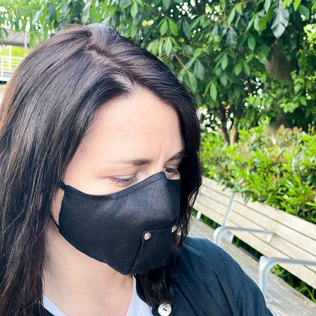 A stylish black face mask made from 100% organic linen, featuring a straw hole for easy sipping, adjustable elastic loops, and a moldable nose bridge.