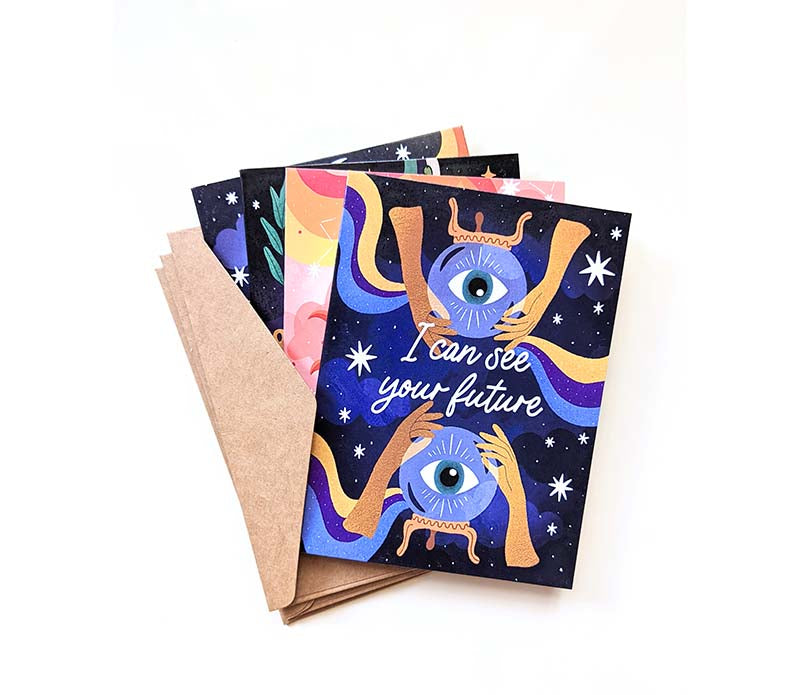 A collection of four Magical Memos Greeting Cards featuring celestial artwork, accompanied by envelopes, displayed on a wooden surface.