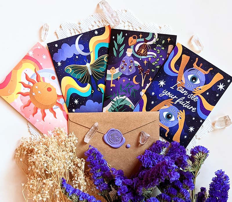 A collection of four Magical Memos Greeting Cards featuring celestial artwork, accompanied by envelopes, displayed on a wooden surface.