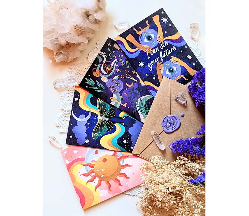 A collection of four Magical Memos Greeting Cards featuring celestial artwork, accompanied by envelopes, displayed on a wooden surface.