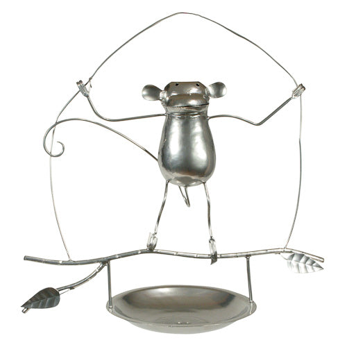 A whimsical metal bird feeder shaped like a monkey, handcrafted from recycled metal, featuring a shallow dish for birdseed.