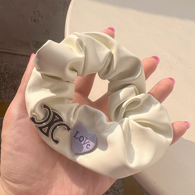 Milky white leather hair tie featuring hearts and bows, elegantly held by a woman's hand.