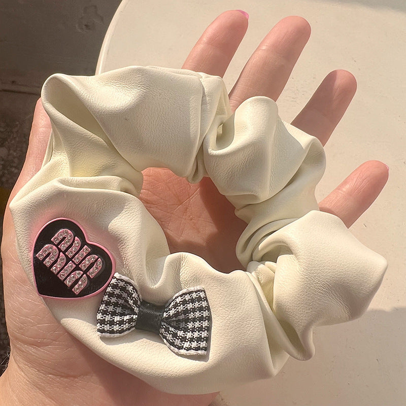 Milky white leather hair tie featuring hearts and bows, elegantly held by a woman's hand.