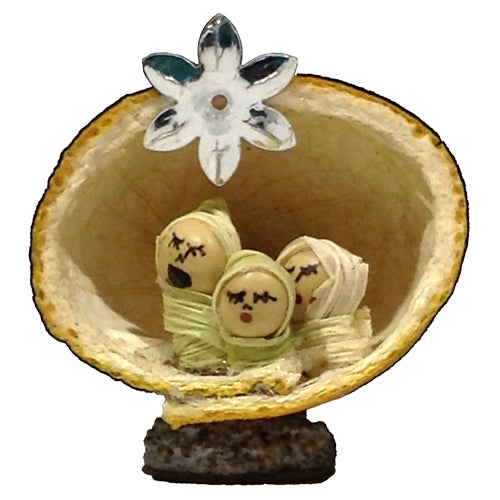 Miniature nativity scene made from orange peel, featuring Mary, Joseph, and Baby Jesus crafted from seeds and corn husk, set on an acorn base.