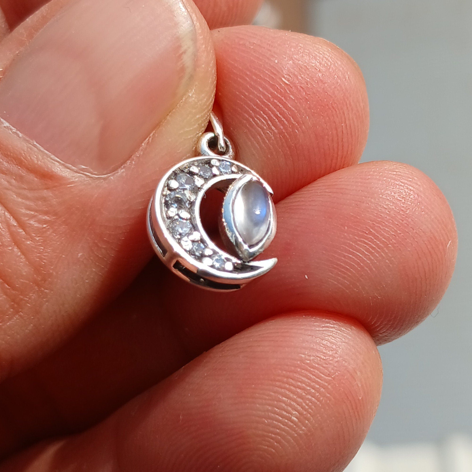 Sterling silver crescent moon pendant featuring a moonstone and cubic zirconias, showcasing its elegant design and craftsmanship.