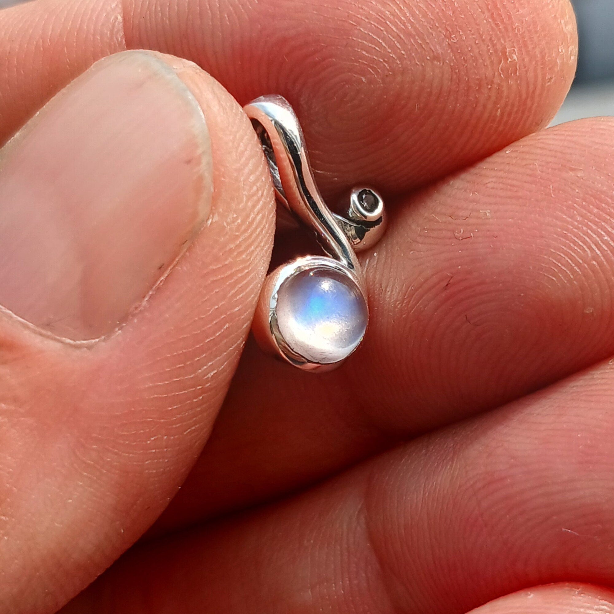 A beautiful Moonstone Pendant featuring a round moonstone charm set in sterling silver, adorned with cubic zirconias, showcasing its iridescent glow.