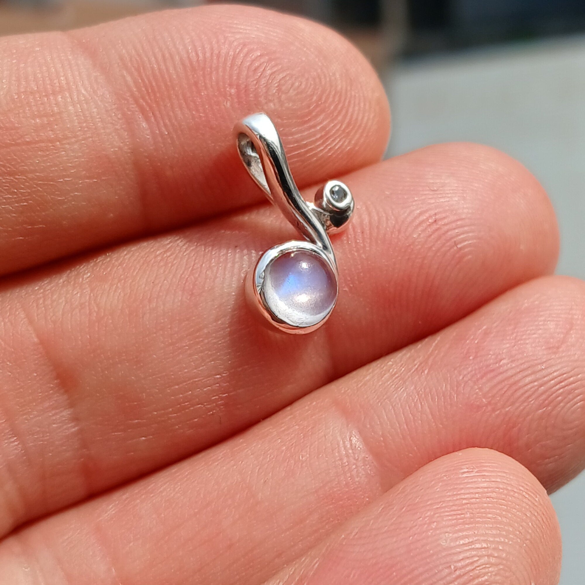 A beautiful Moonstone Pendant featuring a round moonstone charm set in sterling silver, adorned with cubic zirconias, showcasing its iridescent glow.