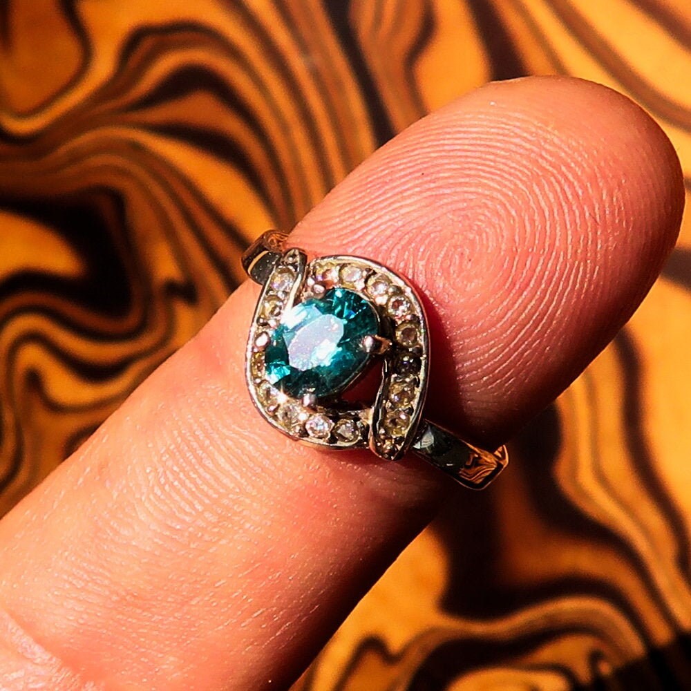 Handmade sterling silver ring featuring a natural oval cut blue Zircon centerpiece surrounded by sparkling CZ stones.