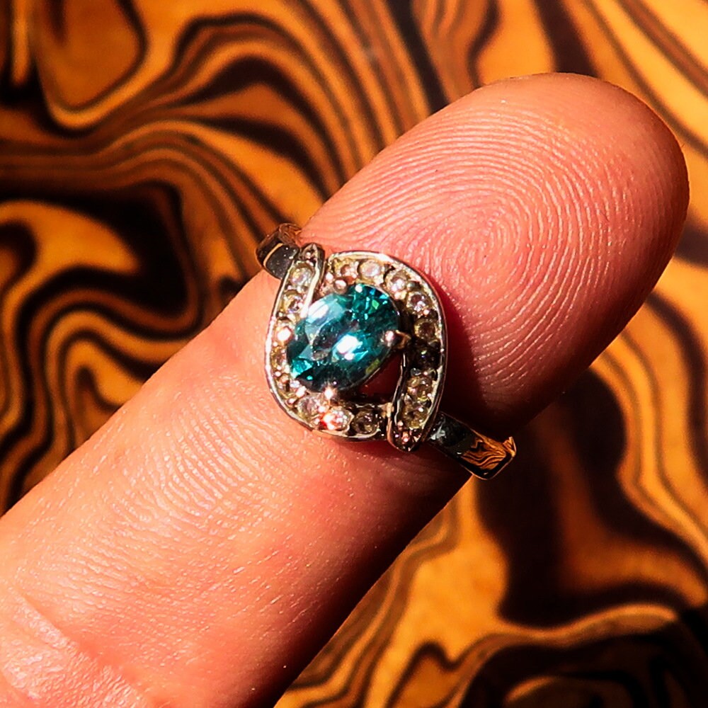 Handmade sterling silver ring featuring a natural oval cut blue Zircon centerpiece surrounded by sparkling CZ stones.