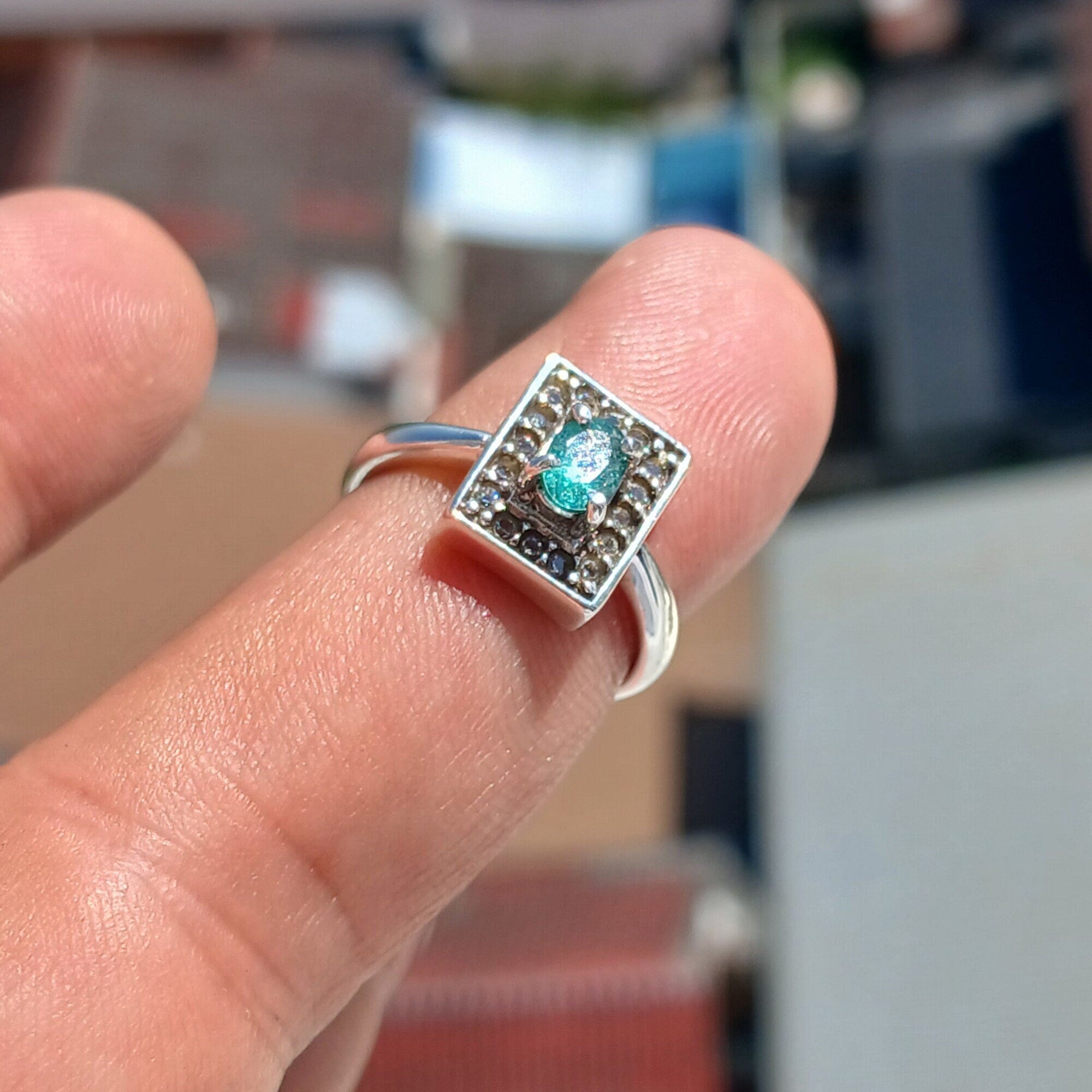 A stunning Natural Emerald Ring featuring an oval cut green emerald surrounded by 16 white cubic zirconia stones, set in polished sterling silver.