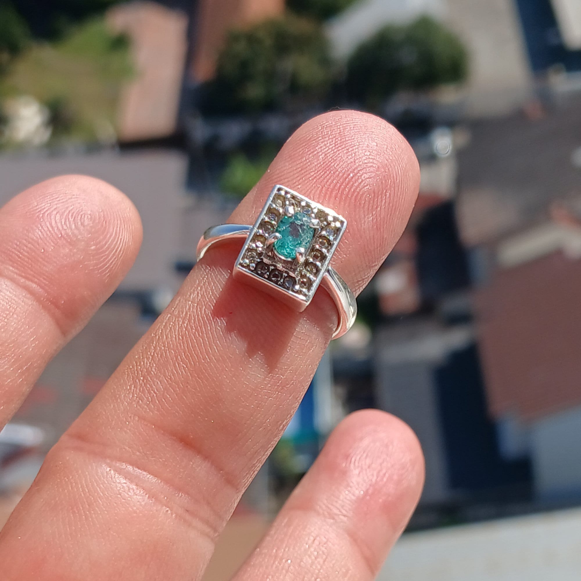 A stunning Natural Emerald Ring featuring an oval cut green emerald surrounded by 16 white cubic zirconia stones, set in polished sterling silver.