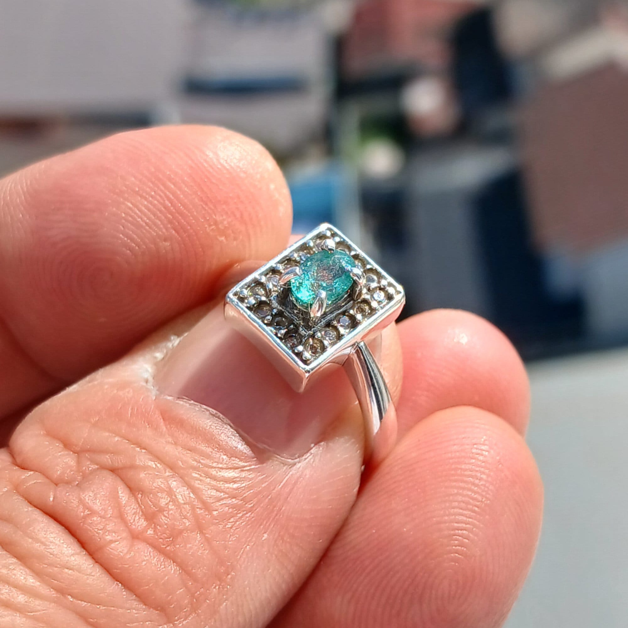 A stunning Natural Emerald Ring featuring an oval cut green emerald surrounded by 16 white cubic zirconia stones, set in polished sterling silver.