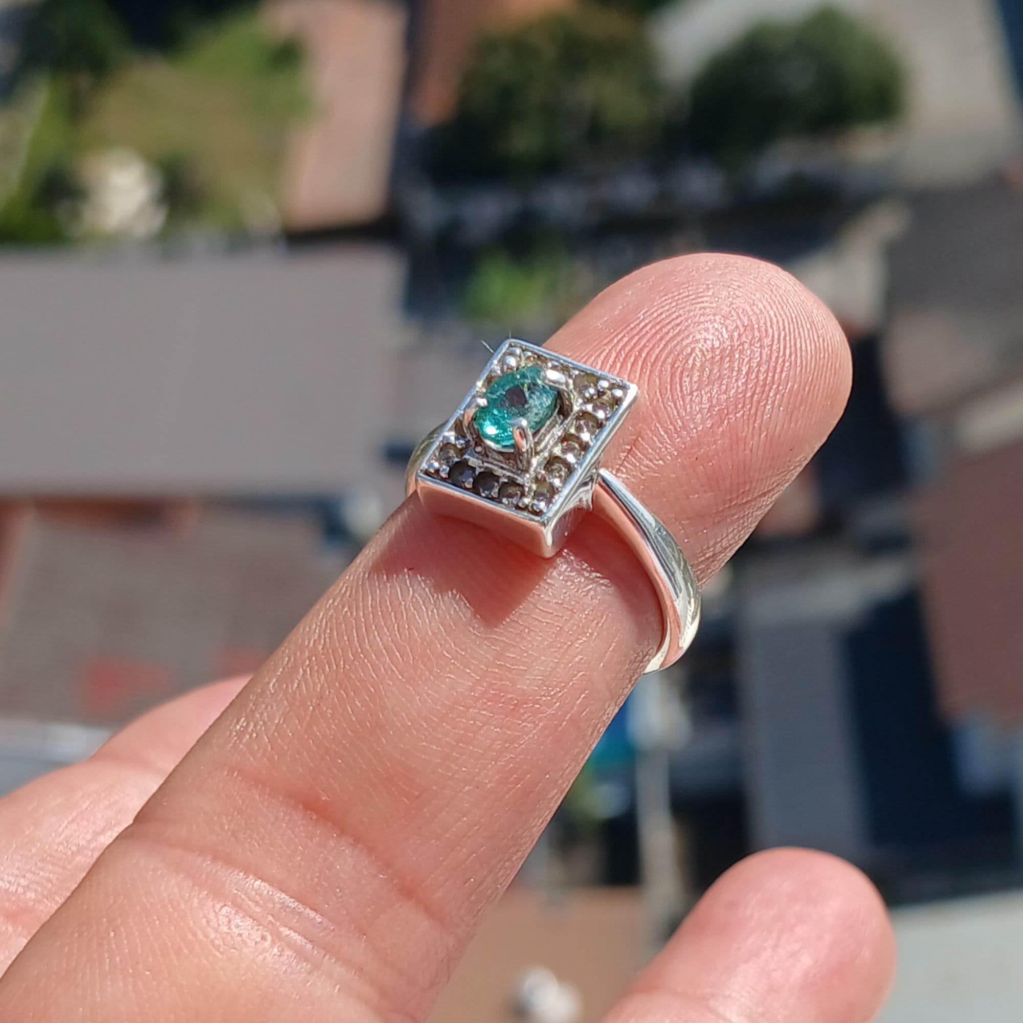 A stunning Natural Emerald Ring featuring an oval cut green emerald surrounded by 16 white cubic zirconia stones, set in polished sterling silver.