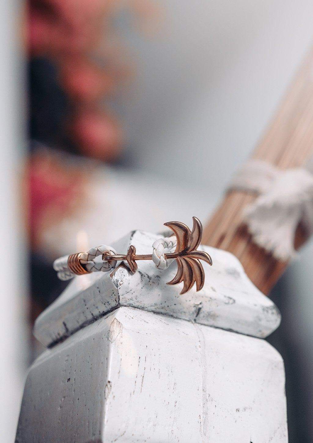 The Palm Band - Paradise Rose featuring a rose gold palm tree charm on a white braided leather bracelet, symbolizing positivity and happiness.