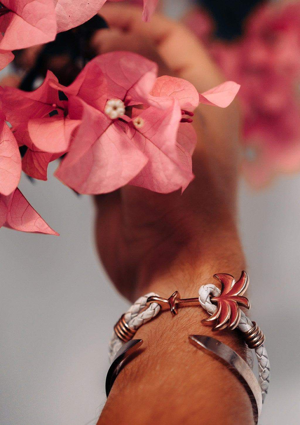 The Palm Band - Paradise Rose featuring a rose gold palm tree charm on a white braided leather bracelet, symbolizing positivity and happiness.