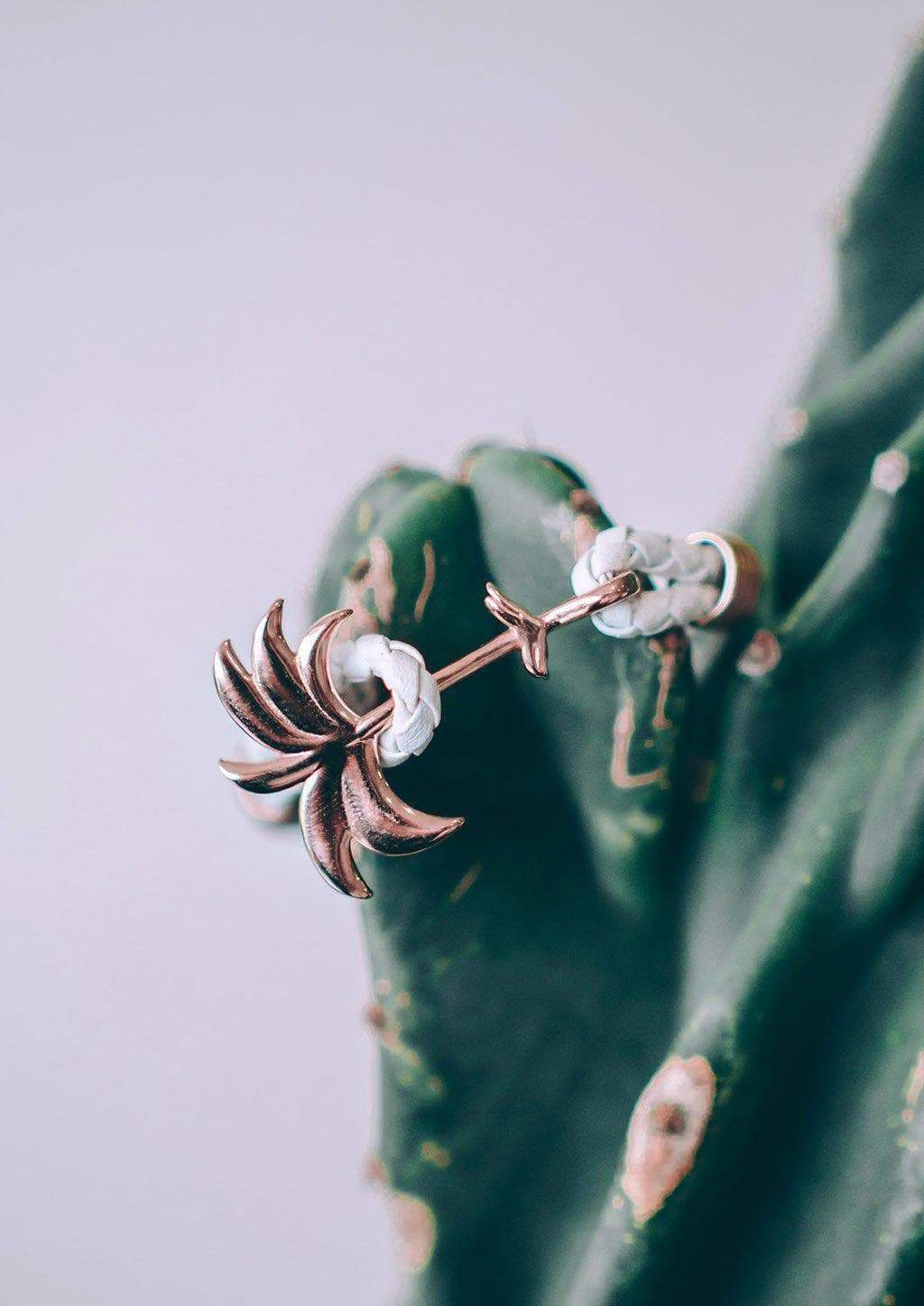 The Palm Band - Paradise Rose featuring a rose gold palm tree charm on a white braided leather bracelet, symbolizing positivity and happiness.