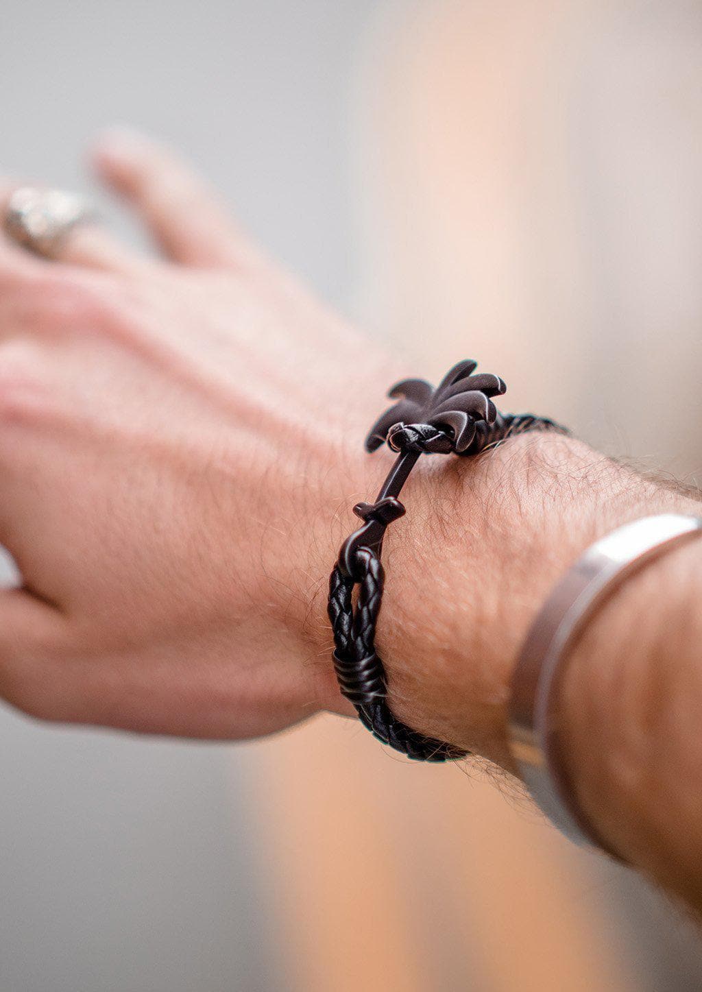 The Palm Band - Pitch Black featuring a matte black palm tree anchor on a thick braided black leather strap, showcasing its modern luxury design.