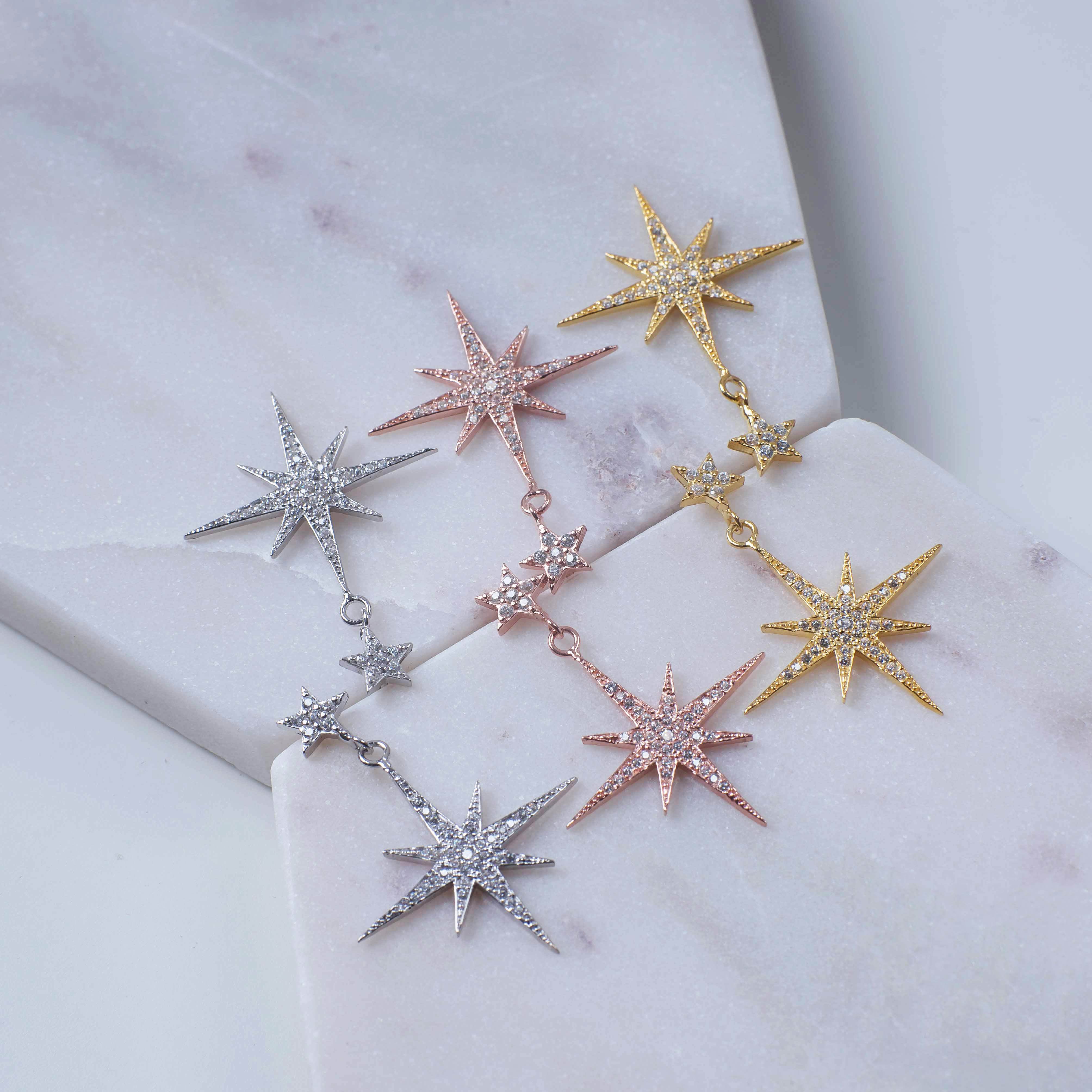 Petite Star Burst Drop Earrings in Gold featuring a larger starburst and smaller stud, adorned with cubic zirconia for a sparkling effect.