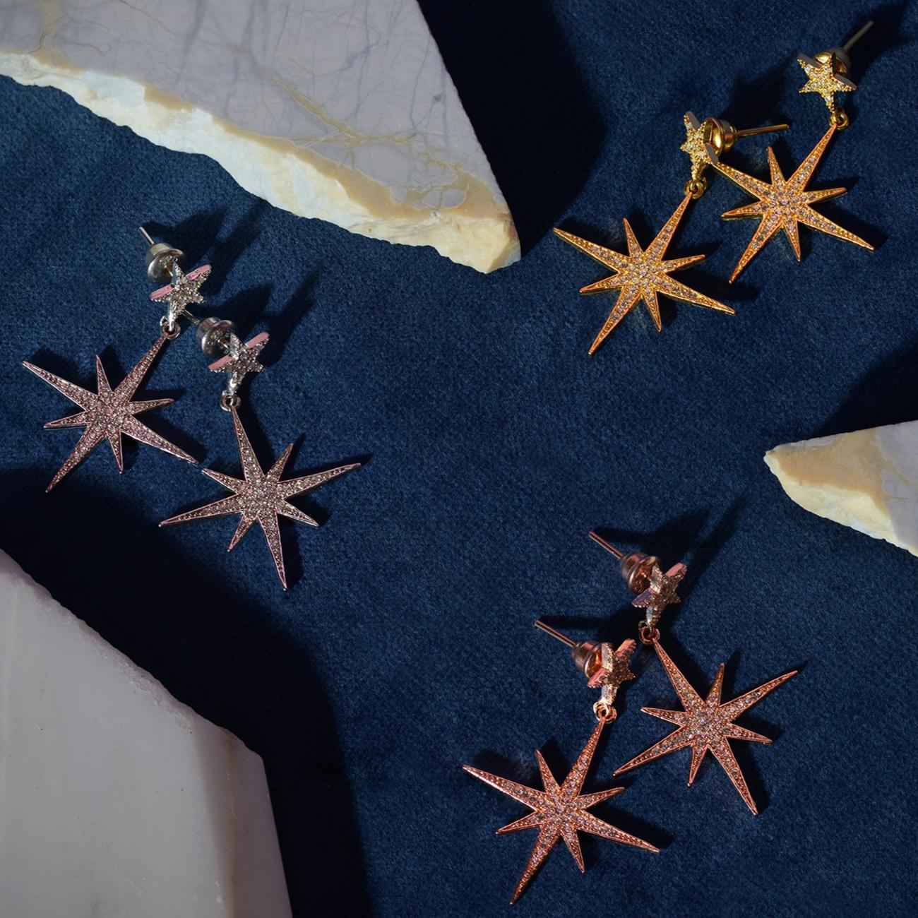 Petite Star Burst Drop Earrings in Gold featuring a larger starburst and smaller stud, adorned with cubic zirconia for a sparkling effect.