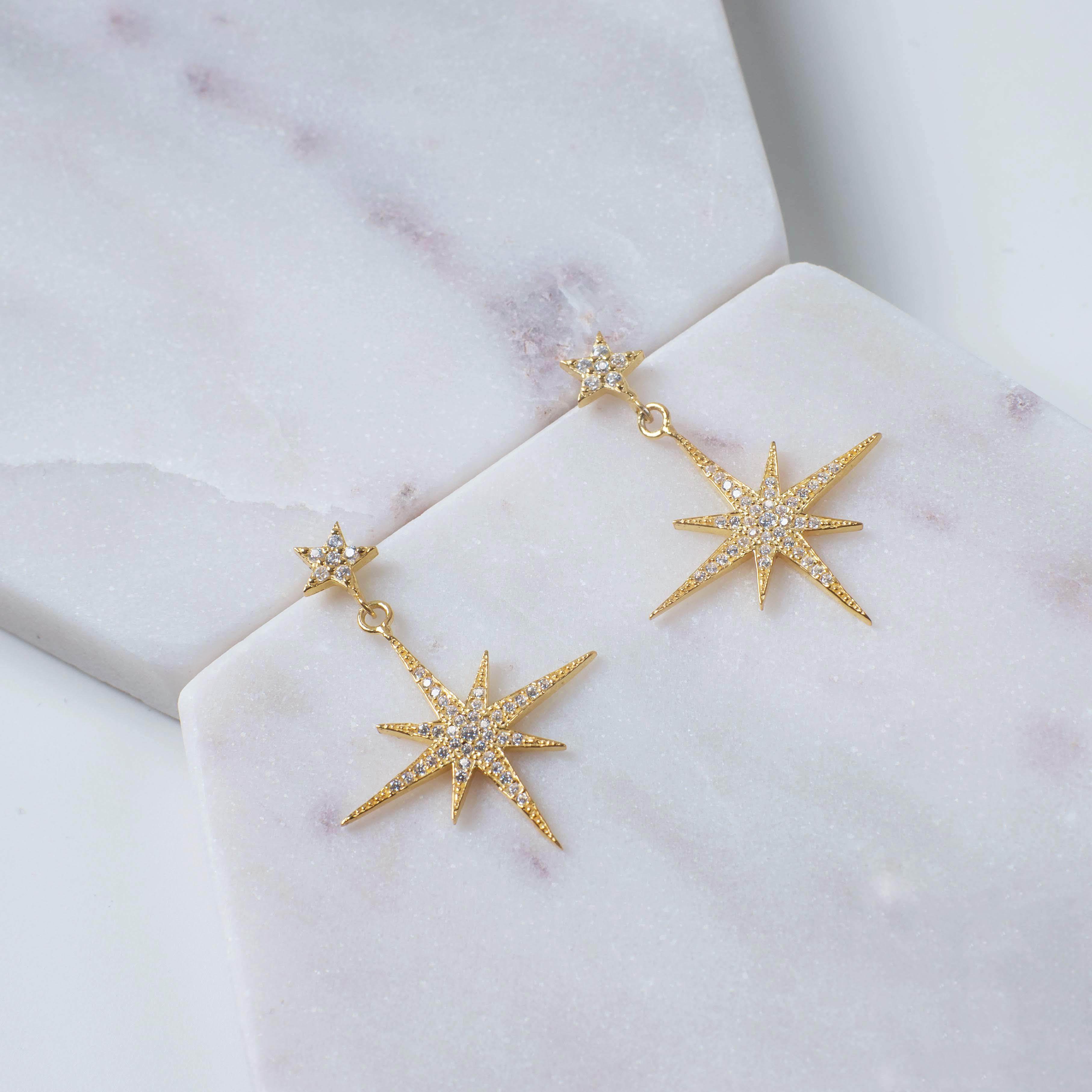 Petite Star Burst Drop Earrings in Gold featuring a larger starburst and smaller stud, adorned with cubic zirconia for a sparkling effect.