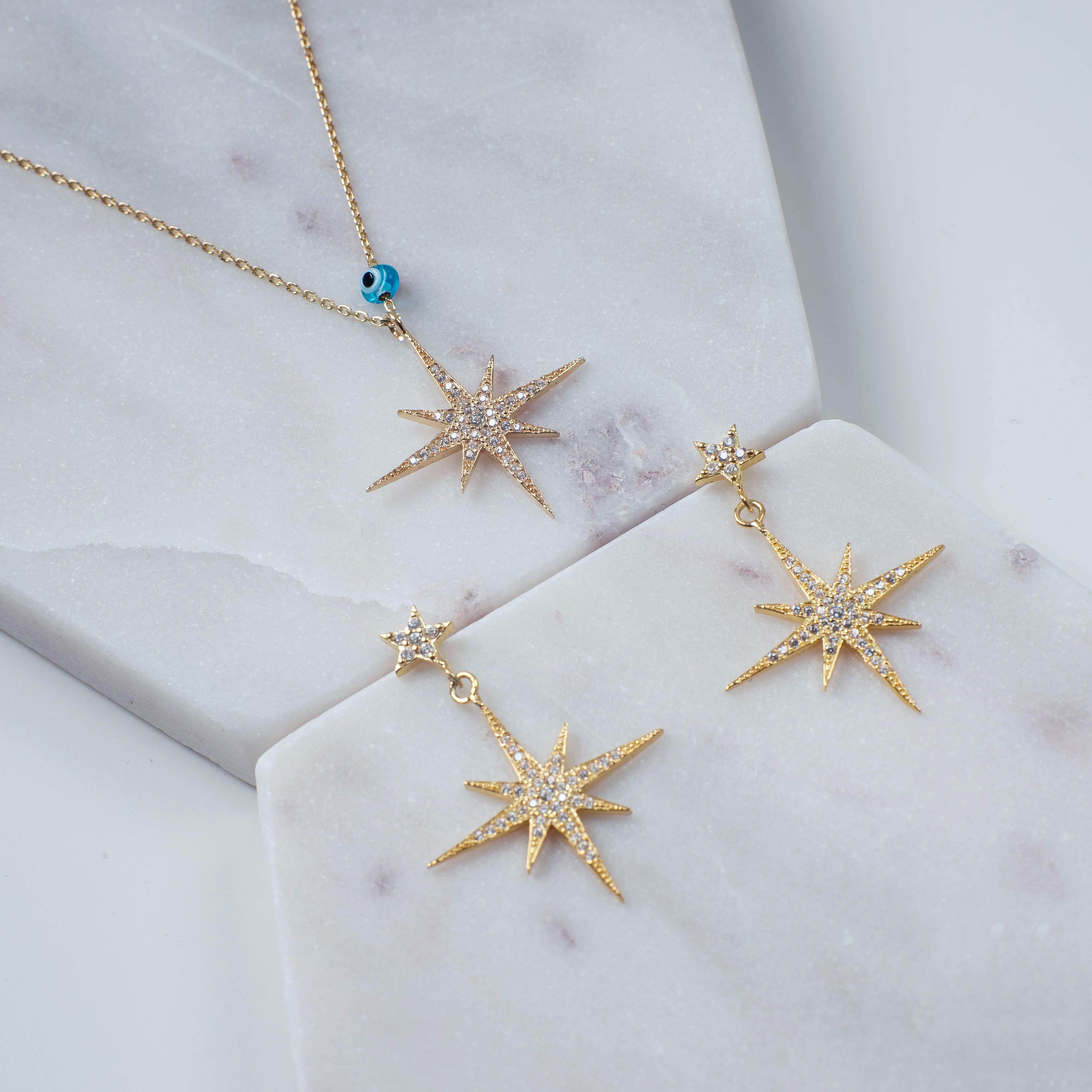 Petite Star Burst Drop Earrings in Gold featuring a larger starburst and smaller stud, adorned with cubic zirconia for a sparkling effect.