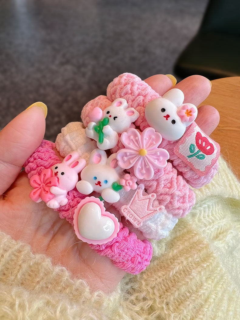 A collection of four pink scrunchies featuring cute animal designs, held by a person, showcasing their stylish and gentle nature.