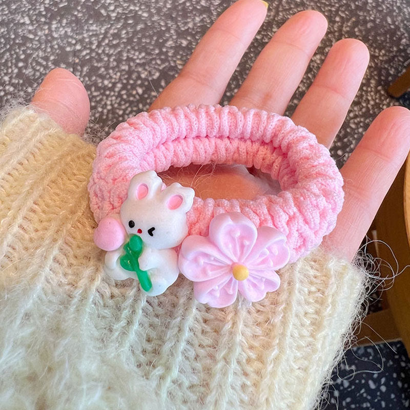 A collection of four pink scrunchies featuring cute animal designs, held by a person, showcasing their stylish and gentle nature.