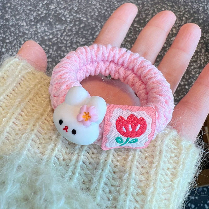 A collection of four pink scrunchies featuring cute animal designs, held by a person, showcasing their stylish and gentle nature.