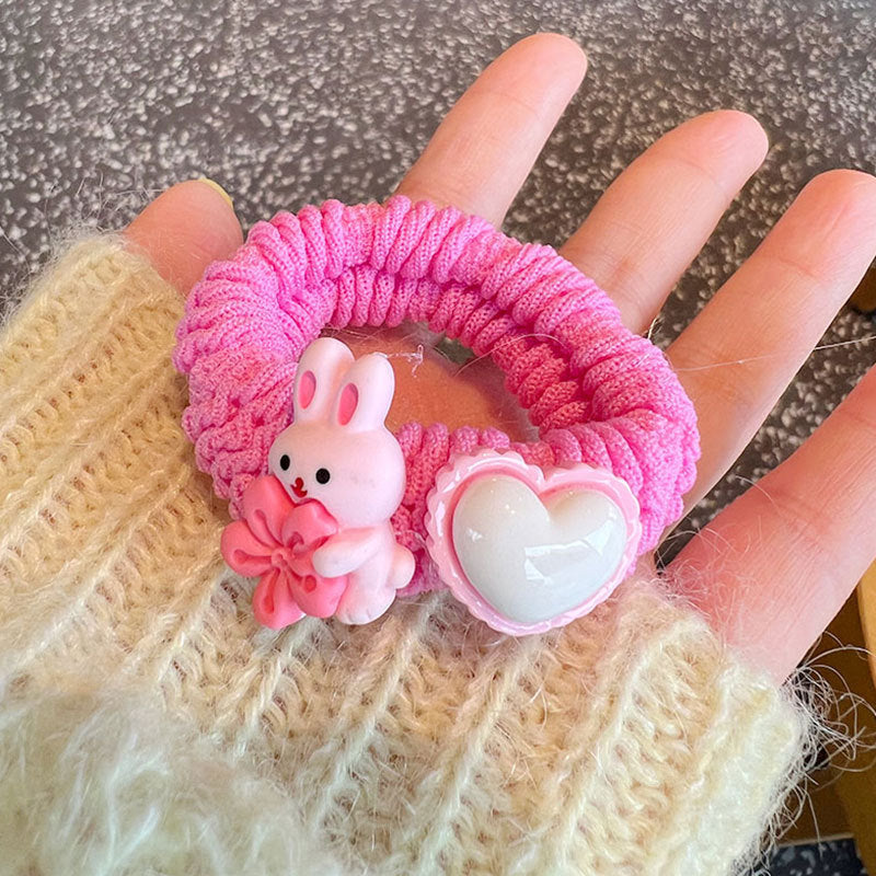 A collection of four pink scrunchies featuring cute animal designs, held by a person, showcasing their stylish and gentle nature.