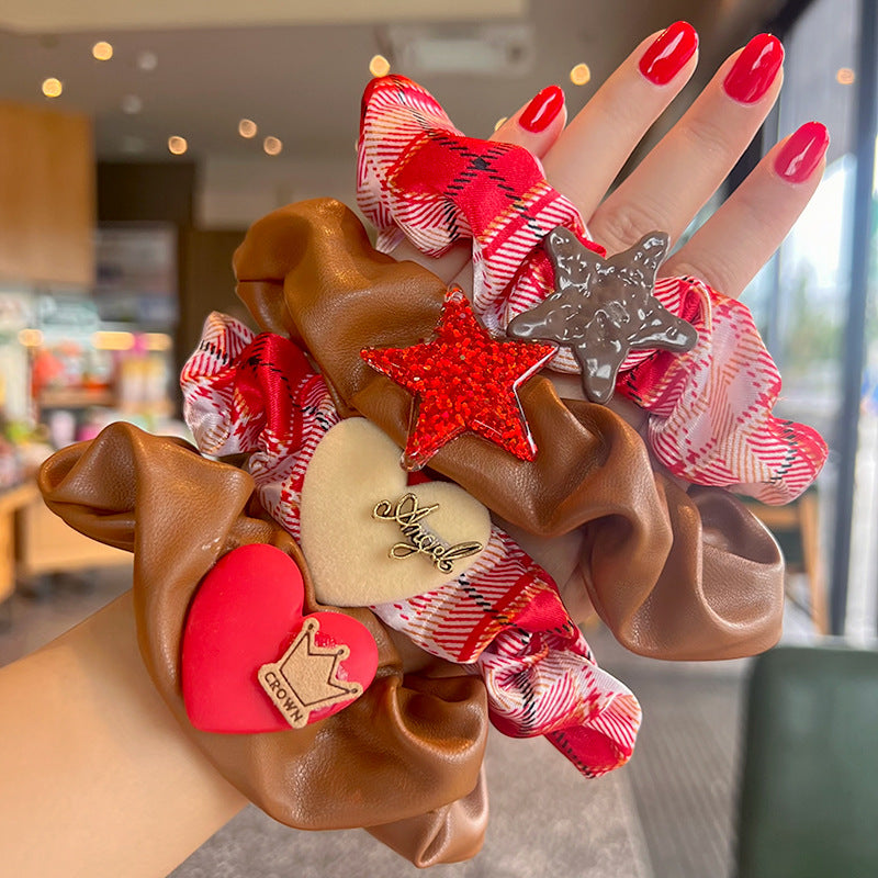 A woman's hand holding a red and white plaid hair tie shaped like a five-pointed star, showcasing its stylish design.