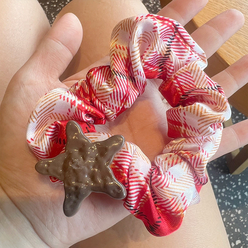 A woman's hand holding a red and white plaid hair tie shaped like a five-pointed star, showcasing its stylish design.