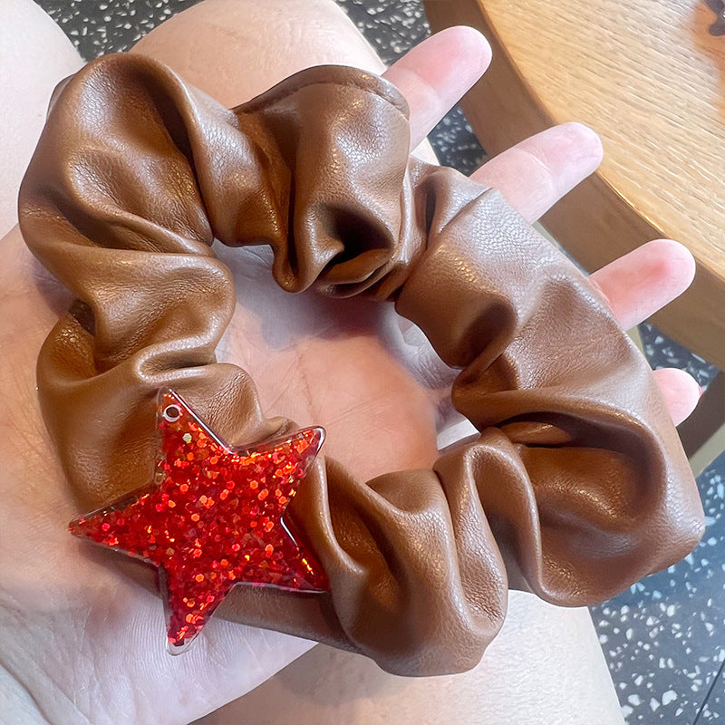 A woman's hand holding a red and white plaid hair tie shaped like a five-pointed star, showcasing its stylish design.