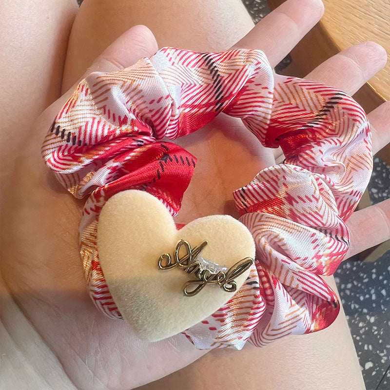 A woman's hand holding a red and white plaid hair tie shaped like a five-pointed star, showcasing its stylish design.