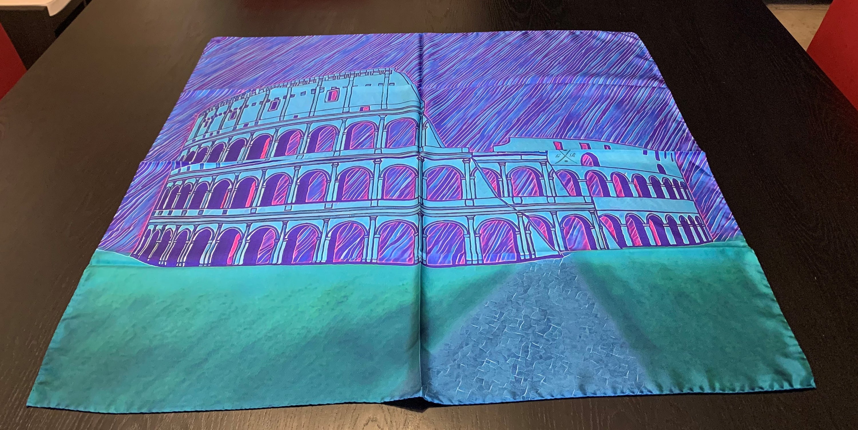 A beautiful blue ladies scarf featuring a sketched image of the Colosseum in Rome, designed with vibrant shades of blue, magenta, and green.