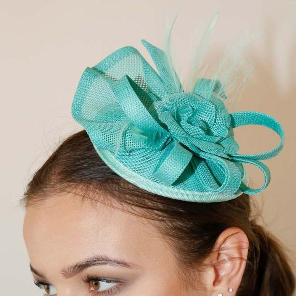 Elegant mint green Ruby Rocks Judeen fascinator featuring a flower design with feathers and a bow, secured with a hair clip.