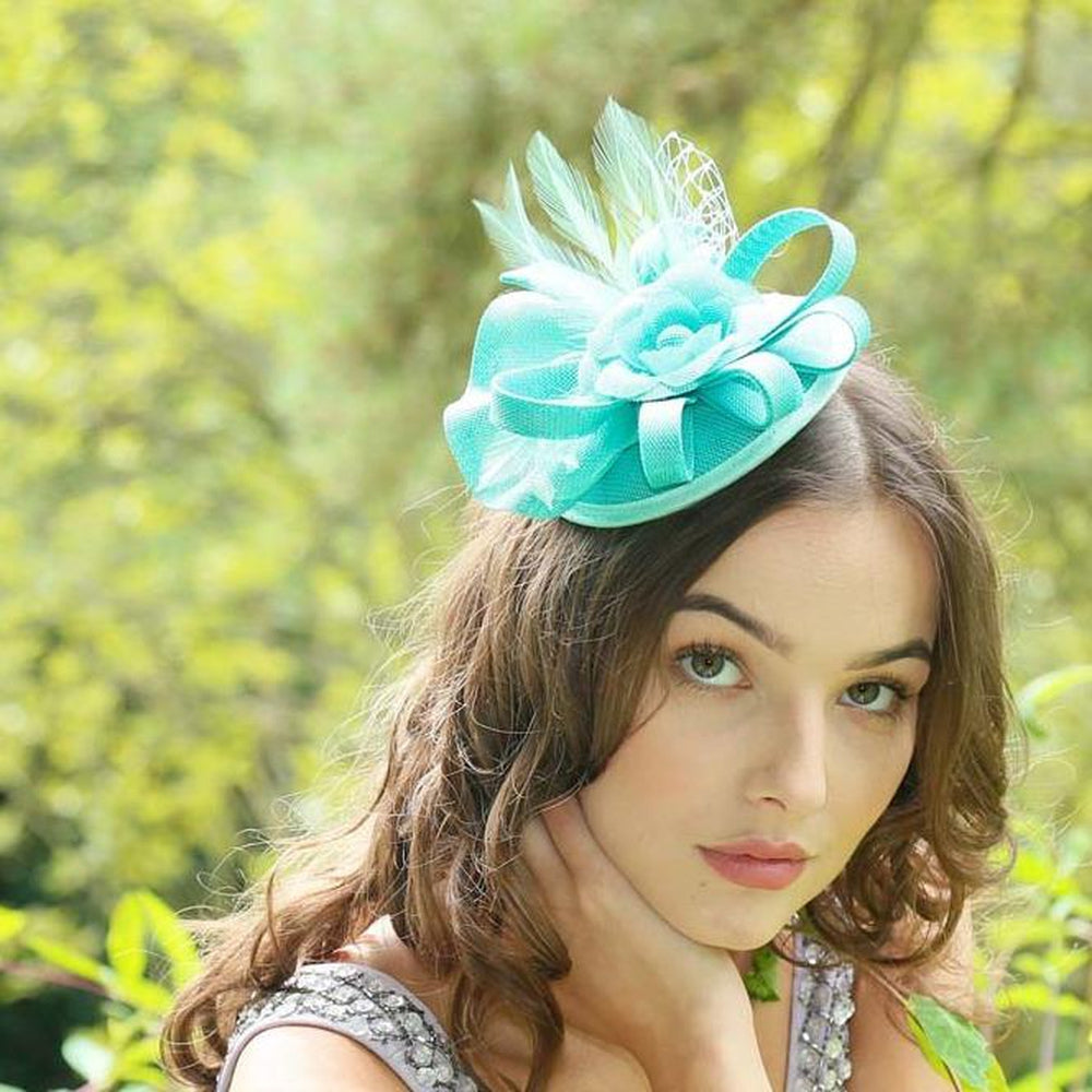 Elegant mint green Ruby Rocks Judeen fascinator featuring a flower design with feathers and a bow, secured with a hair clip.