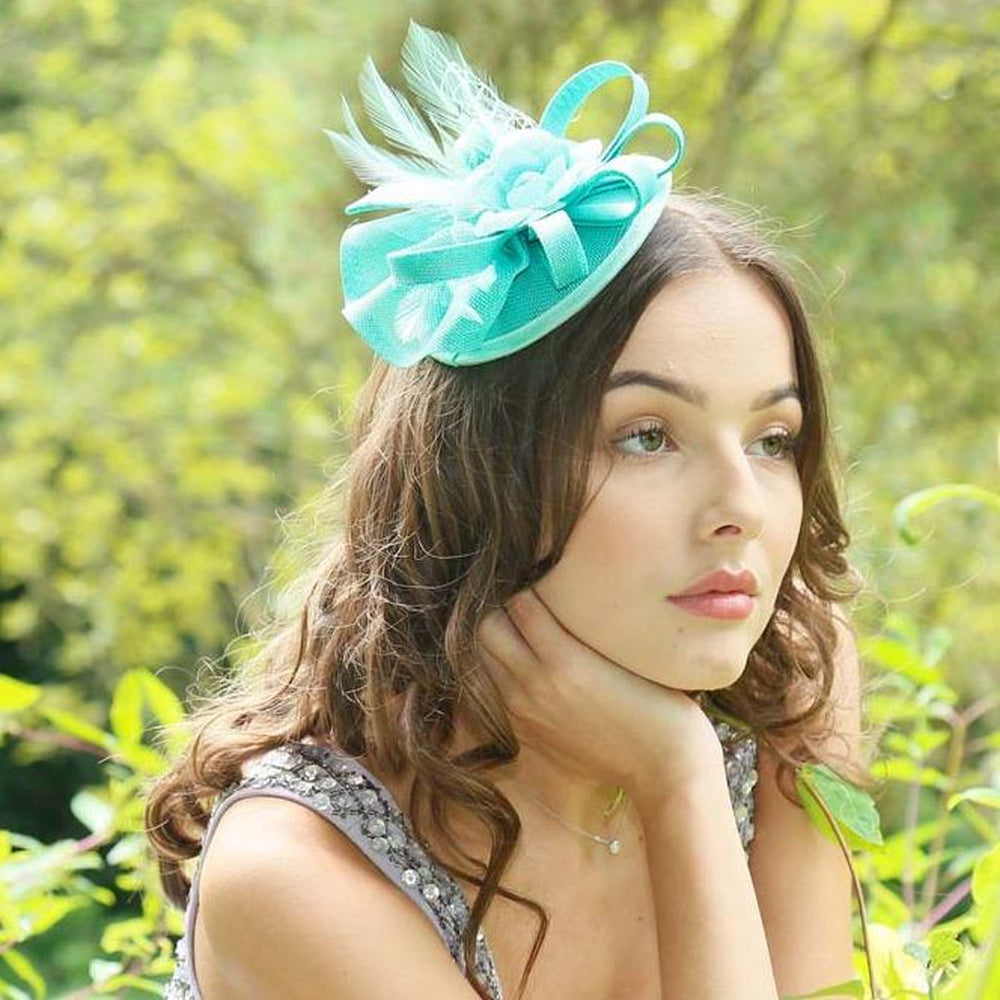 Elegant mint green Ruby Rocks Judeen fascinator featuring a flower design with feathers and a bow, secured with a hair clip.