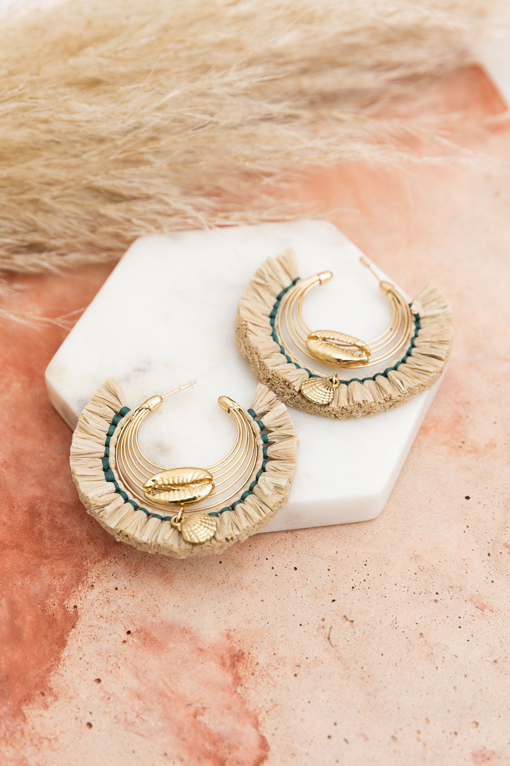 A pair of Seashell Raffia Earrings featuring delicate hoops adorned with shimmering seashells and golden raffia, showcasing coastal elegance.