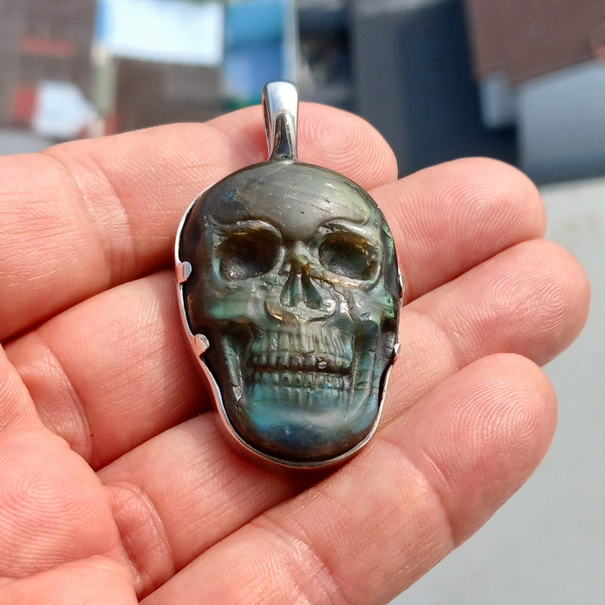 Handcrafted sterling silver skull pendant featuring a Labradorite carving, polished to a mirror finish, showcasing intricate details.