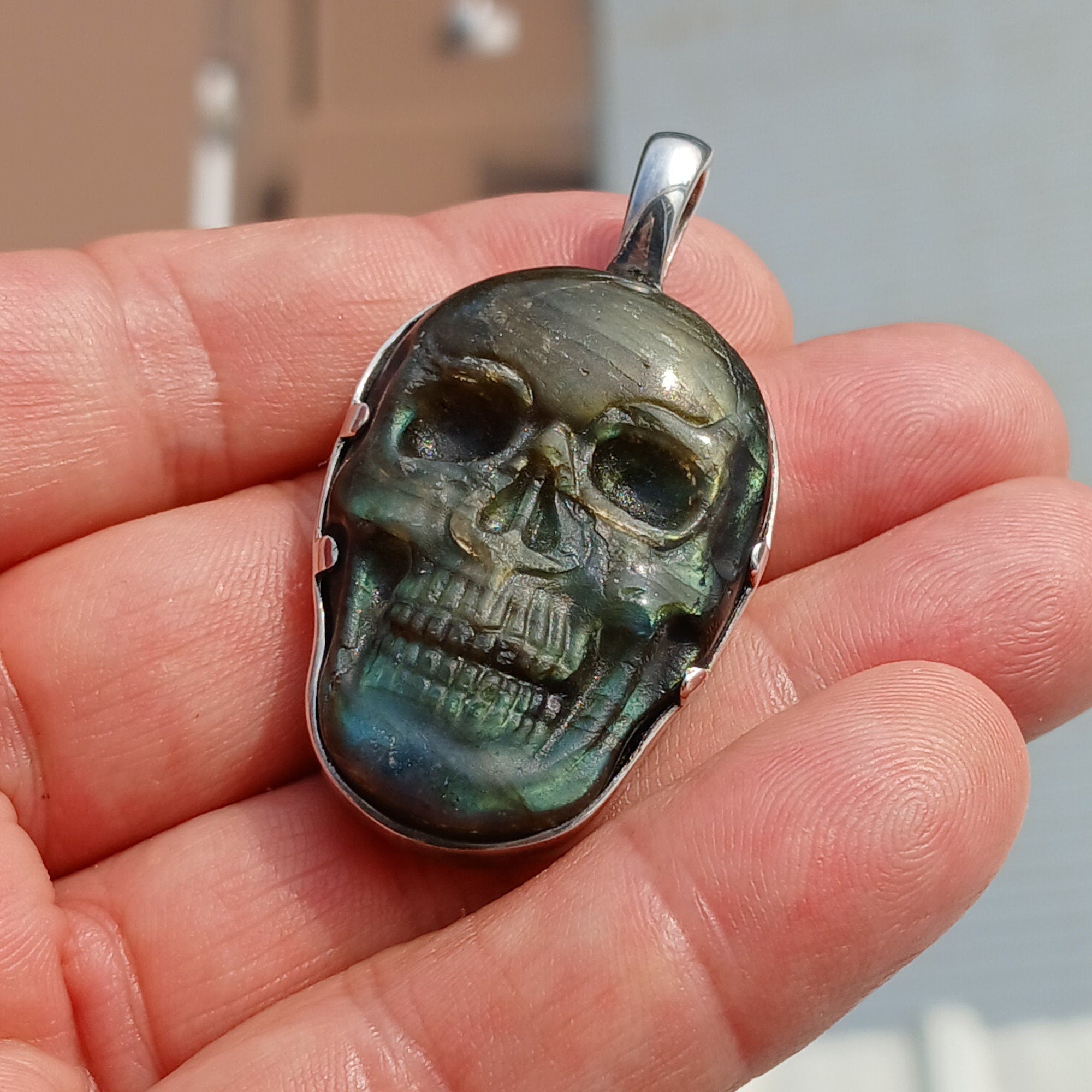 Handcrafted sterling silver skull pendant featuring a Labradorite carving, polished to a mirror finish, showcasing intricate details.