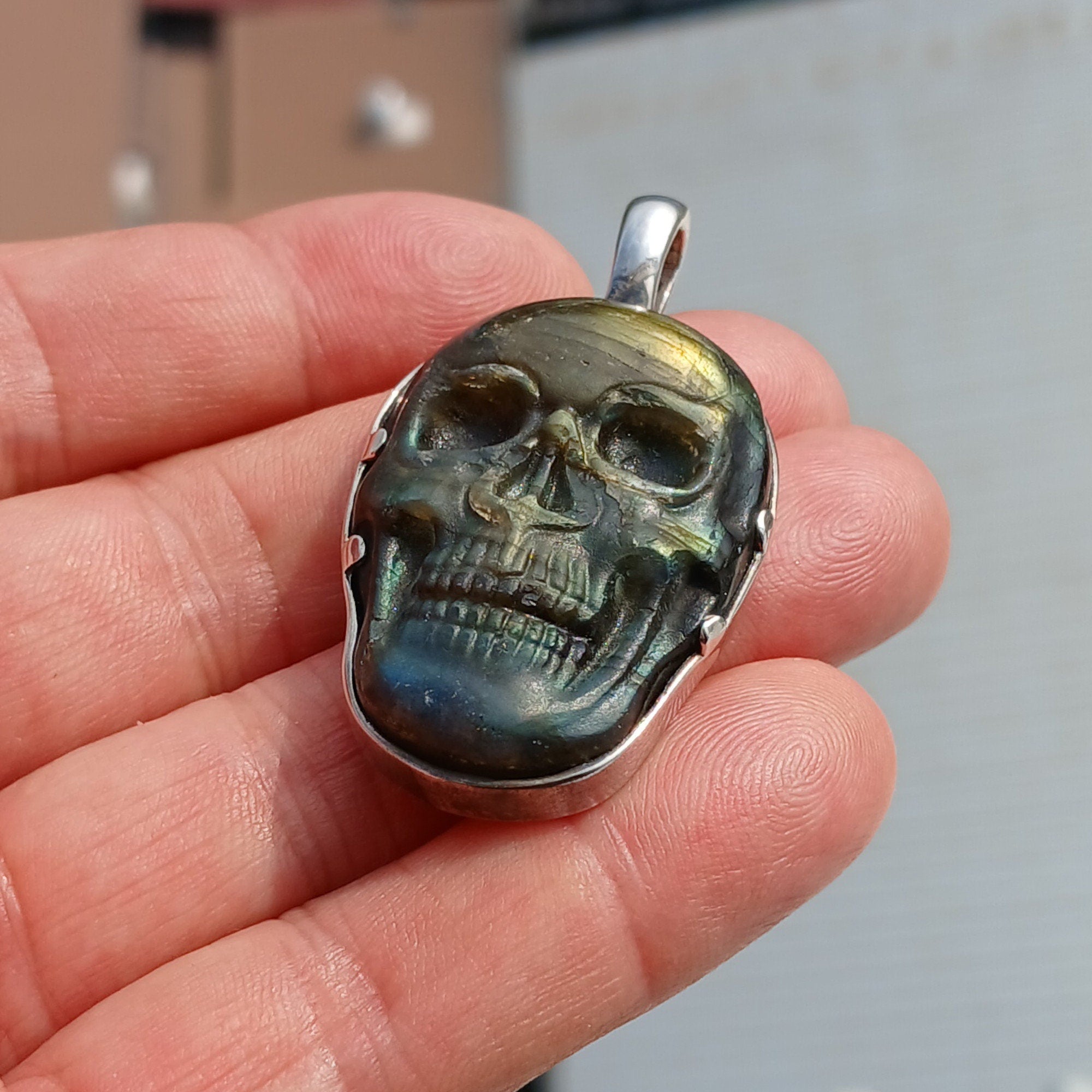 Handcrafted sterling silver skull pendant featuring a Labradorite carving, polished to a mirror finish, showcasing intricate details.