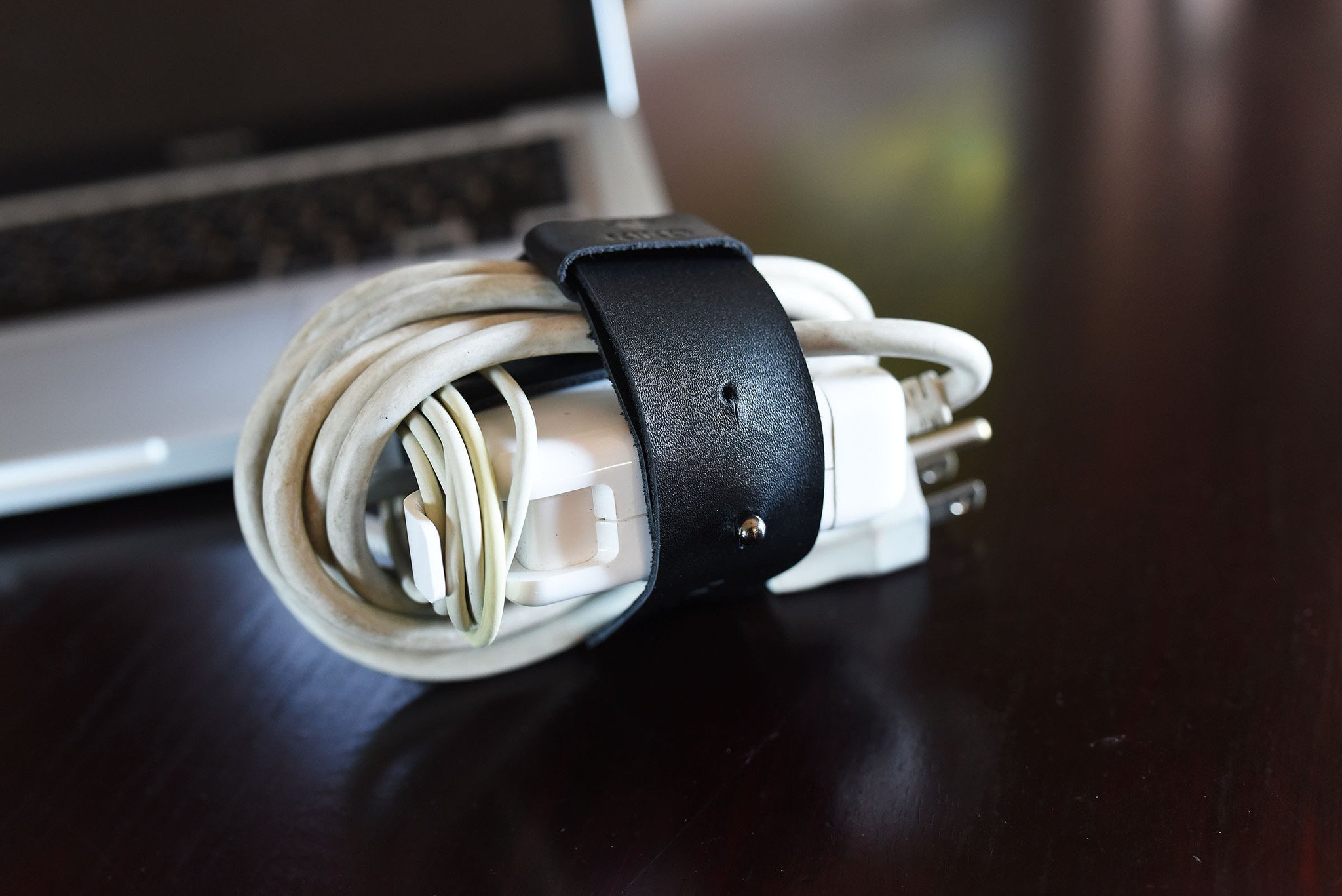 The Mac Cord Lord, a stylish leather cord organizer for MacBook chargers, featuring an adjustable cross-strap design.