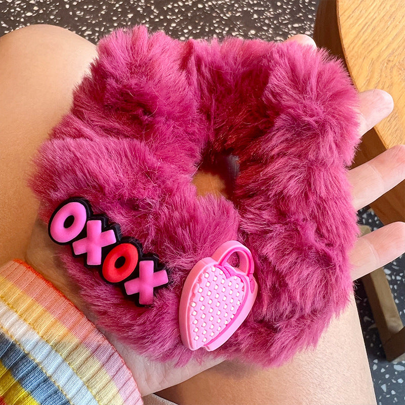 A woman's hand holding four pink fuzzy scrunchies, showcasing their soft texture and stylish design.