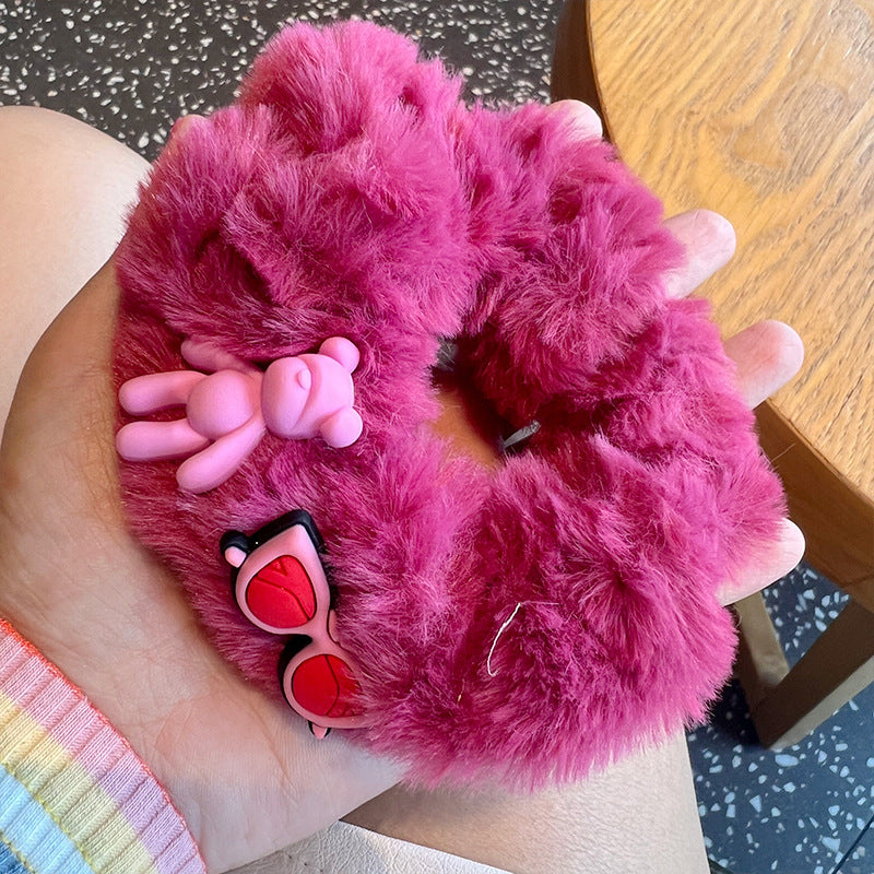 A woman's hand holding four pink fuzzy scrunchies, showcasing their soft texture and stylish design.