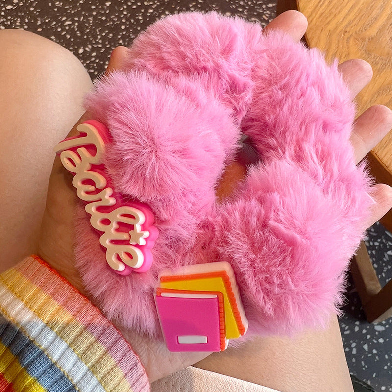 A woman's hand holding four pink fuzzy scrunchies, showcasing their soft texture and stylish design.