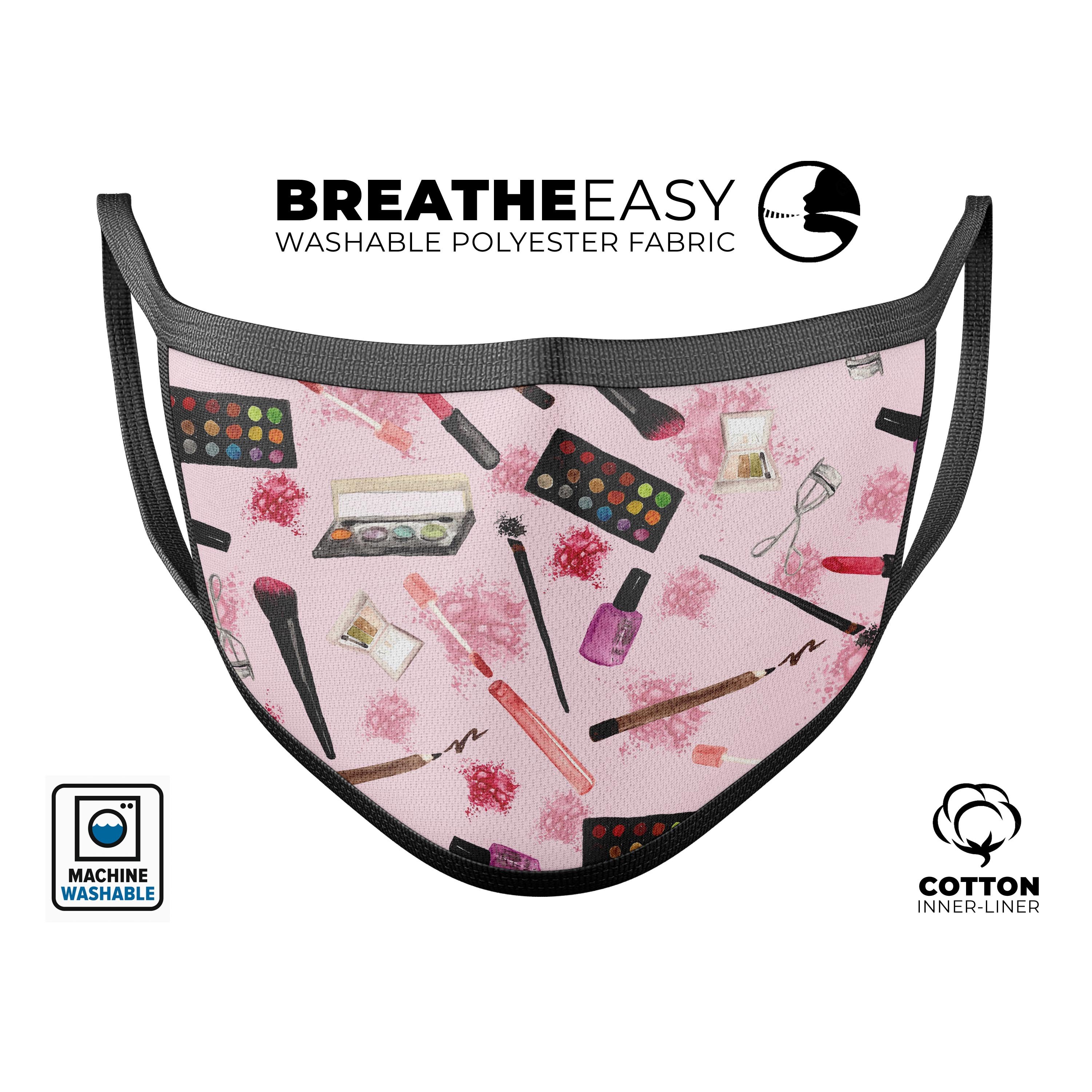 A vibrant pink face mask featuring a makeup bag pattern, made in the USA, showcasing adjustable ear loops and a soft cotton interior.