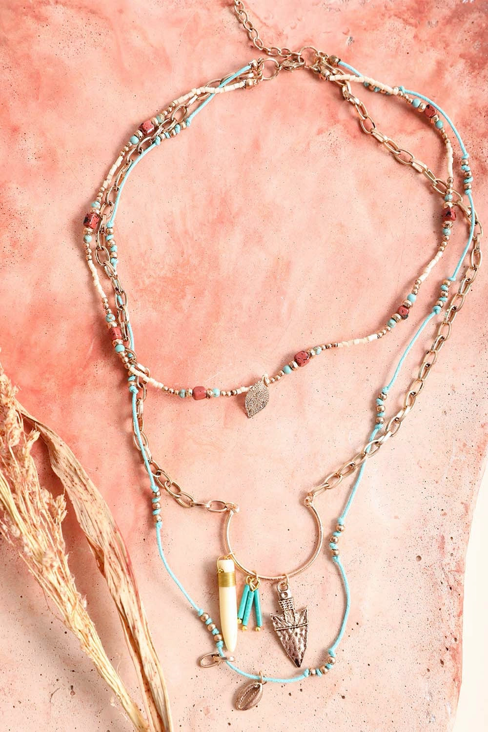 A layered necklace featuring a tusk horn pendant and an arrow charm on a delicate chain, showcasing a whimsical and elegant design.