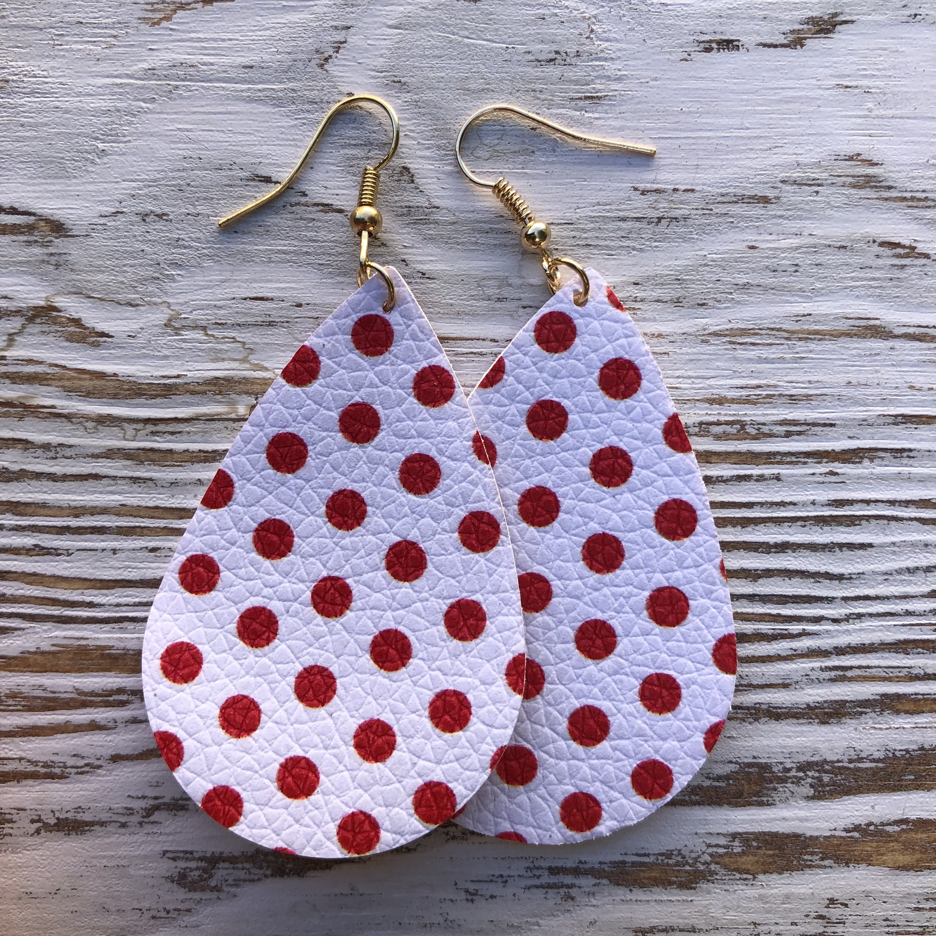 A pair of lightweight white and red polka dot leather earrings with a fish hook closure, showcasing a playful and stylish design.