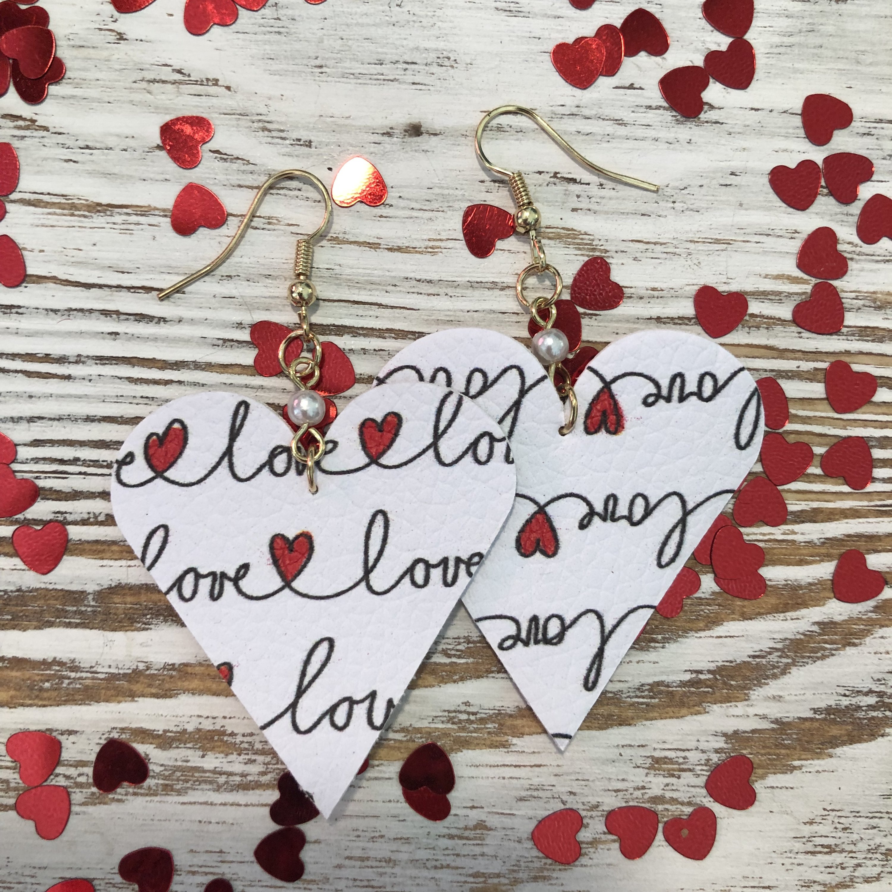 A pair of White Love Scrawled Mini Heart Leather Pearl Earrings featuring a lightweight design and elegant fish hook style.